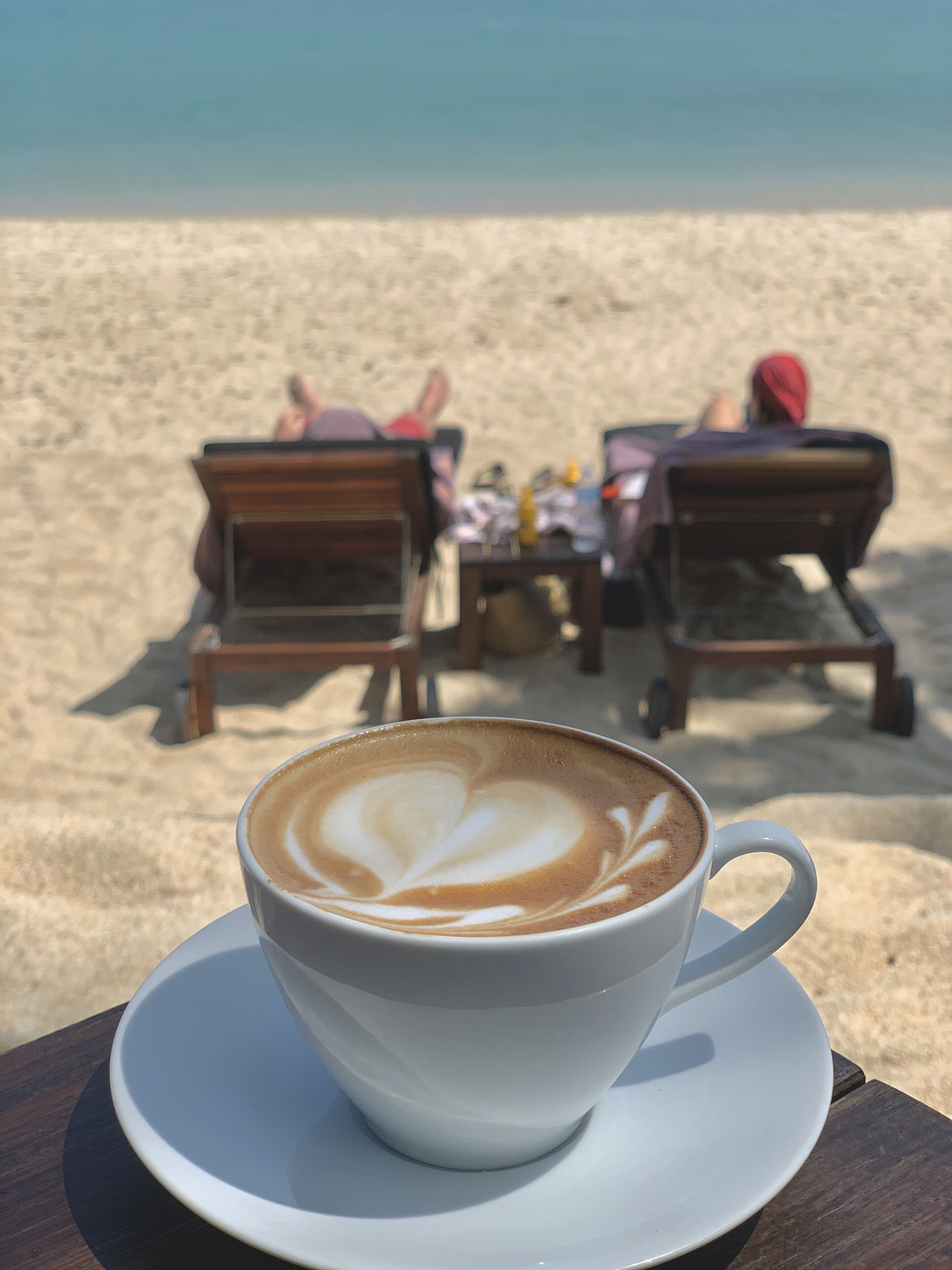 A cup of coffee with latte art on a saucer, placed on a wooden table.