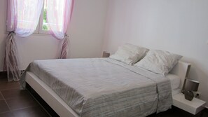 A bedroom with a bed, curtains, a bedside table, and a nightstand. - EDEN BLUE THE DREAM FEET IN THE WATER (SAINTE ANNE)