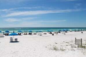 A beach with white sand, blue umbrellas, and wooden lounge chairs. - Steps to the Beach, Family Friendly, No Elevators or Parking Deck hassle (Panama City Beach)