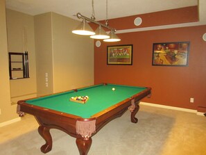 A pool table with balls, a hanging light fixture, and two framed pictures on the wall.