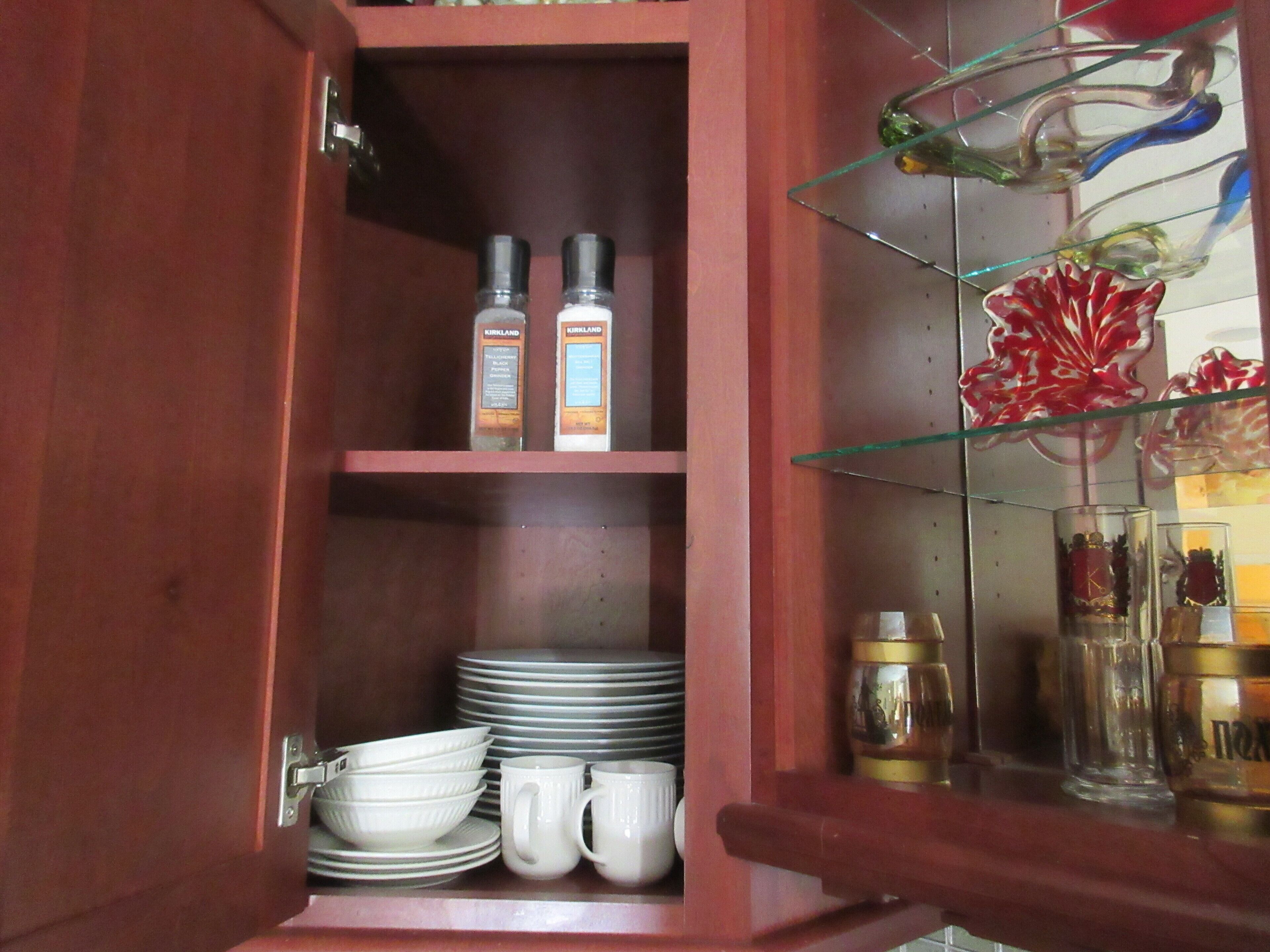 A wooden cabinet with shelves containing kitchenware, including plates, bowls, and mugs.