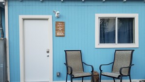 A blue building with a white door, two chairs, a wooden sign, and a window.