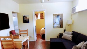 A room with a wooden dining table, chairs, a sofa, a TV, and a painting on the wall.