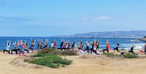 A group of people performing yoga on a beach with a pier in the background.