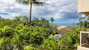 A lush garden with palm trees and a view of the ocean. - Maui Banyan - Ocean View G Condo (Kihei)
