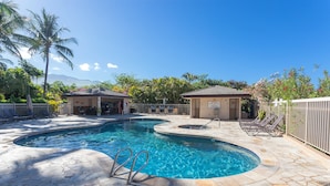 A pool area with a curved design, lounge chairs, and a small building. - Maui Banyan - Ocean View G Condo (Kihei)