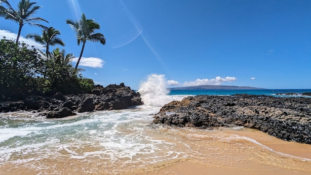 A beach with rocky terrain, palm trees, and waves crashing onto the shore. - Maui Banyan - Ocean View G Condo (Kihei)