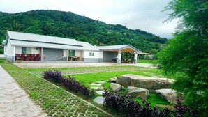 Un edificio de dos pisos con techo plano, un área de estar al aire libre cubierta y un patio empedrado con piedras.