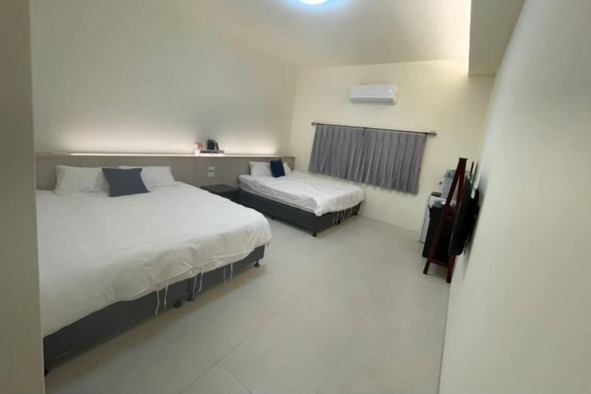 Ein Hotelzimmer mit zwei Betten, einem Nachttisch, einem kleinen Schreibtisch, einem Stuhl und einem Fenster mit Vorhängen.