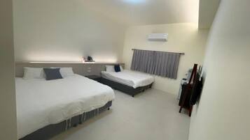 A hotel room with two beds, a bedside table, a small desk, a chair, and a window with curtains.