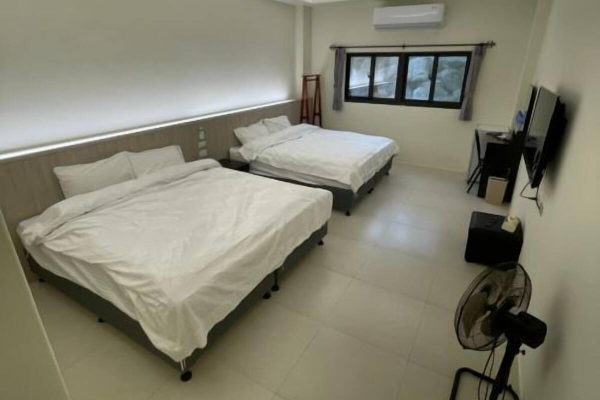 Ein Hotelzimmer mit zwei Betten, einem Fernseher, einem Ventilator und einem Fenster mit Vorhängen.