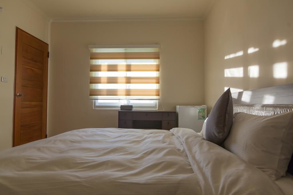 A bedroom with a bed, a nightstand, a window with blinds, and a door.