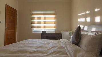 A bedroom with a bed, a nightstand, a window with blinds, and a door.