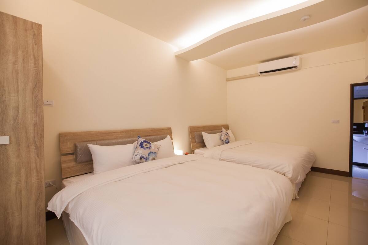 Ein Hotelzimmer mit zwei Betten, einem Holzkopfstück, einer Wand-Klimaanlage und einer Tür rechts.