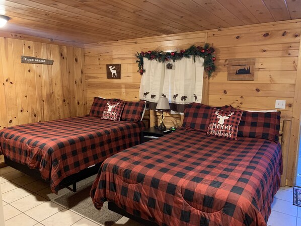 A cozy room with two beds, each with a red and black checkered bedspread and matching pillows, a nightstand with a lamp, and a sign indicating a tree stand.