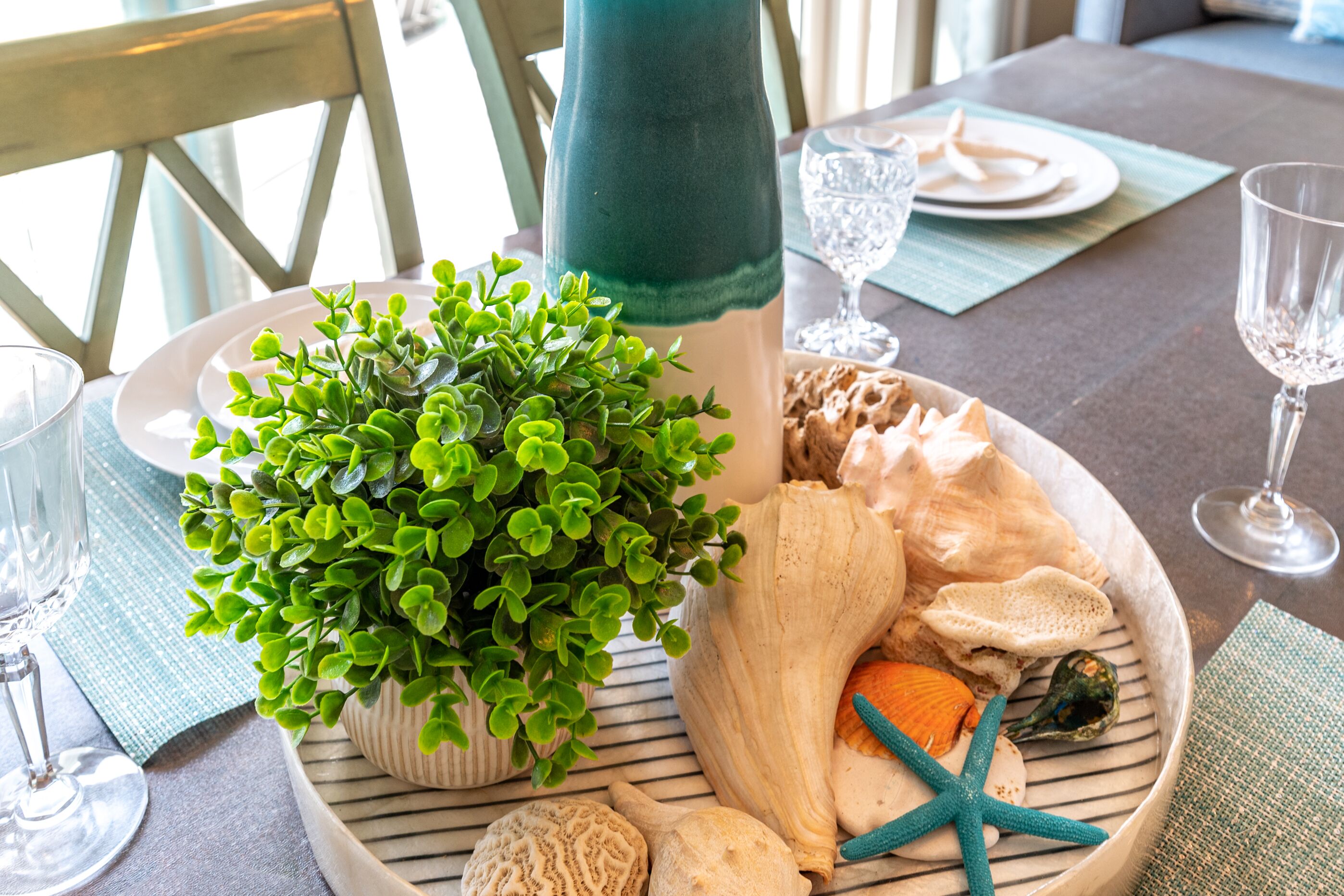 A dining table with a potted plant, seashells, starfish, and a striped placemat.