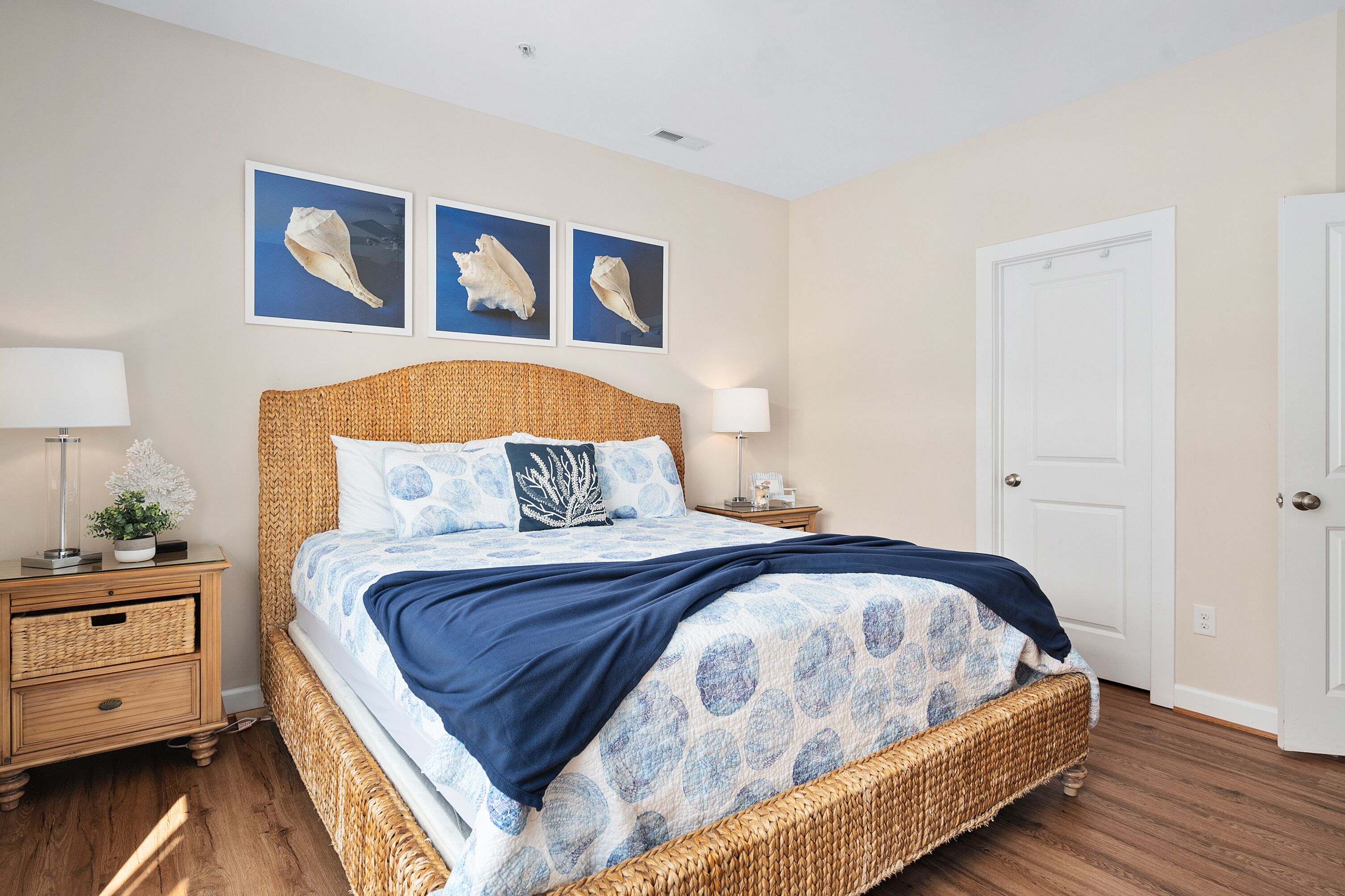 A bedroom with a wicker bed, two nightstands, a door, and three framed pictures on the wall.