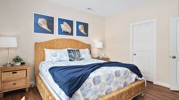A bedroom with a wicker bed, two nightstands, a door, and three framed pictures on the wall.