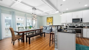 Una cocina moderna con gabinetes blancos, electrodomésticos de acero inoxidable y una zona de comedor de madera con un banco.