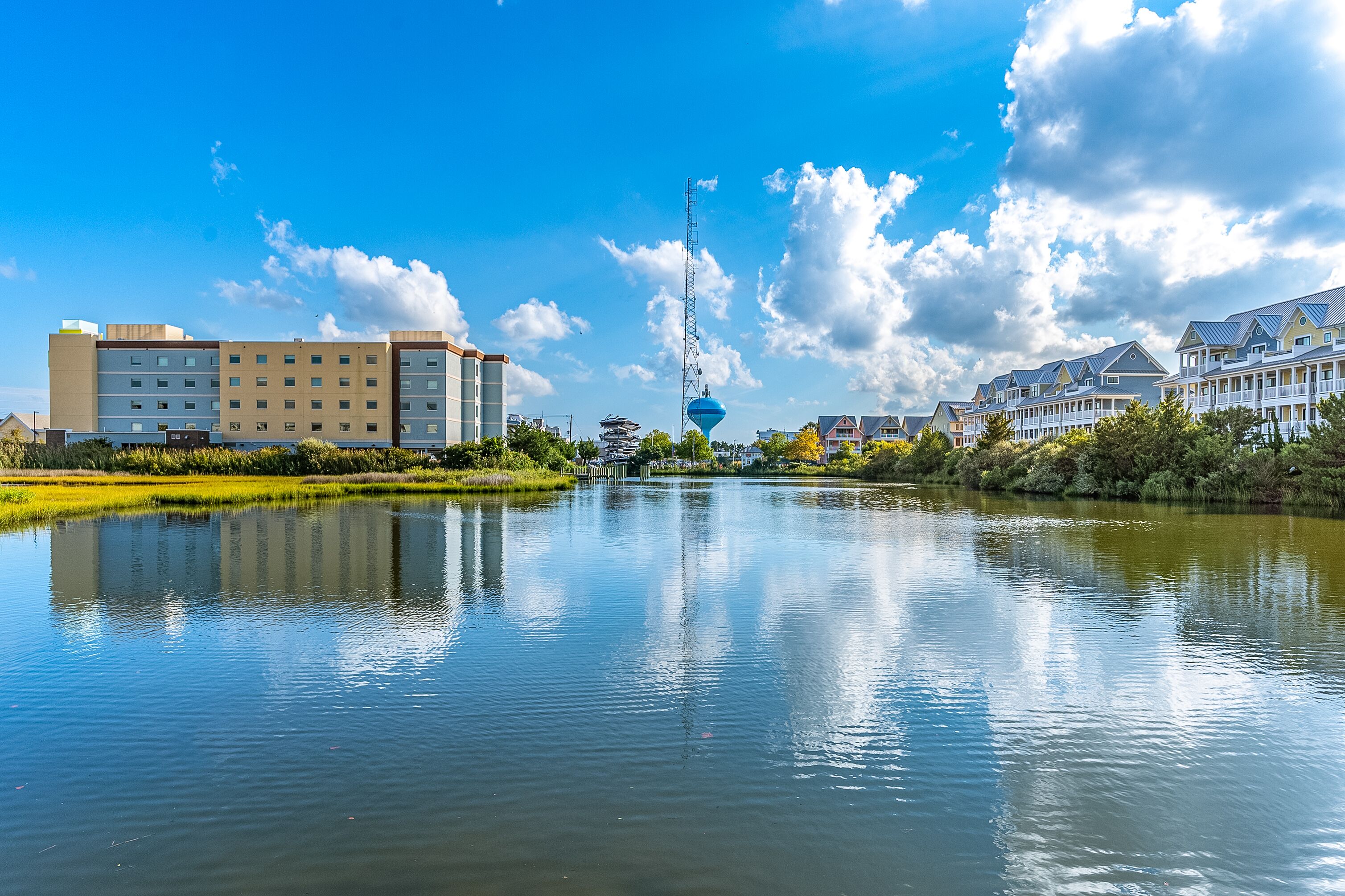 A hotel with a large building, a water body in front, and a tower in the background.