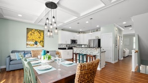 Una cocina moderna con armarios blancos, una isla central y un comedor con mesa de madera y sillas de mimbre.