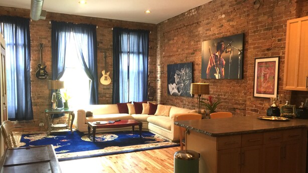 A living room with a brick wall, a sofa, a coffee table, and a small kitchen area with a sink and cabinets.