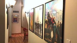 A hallway with framed posters on the wall, a red chair, and a light fixture.