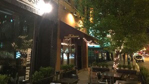 An outdoor dining area with tables and chairs, a sign for Bistro Voltaire, and a street with cars and lights in the background.