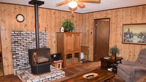 Un salon chaleureux avec une cheminée en briques, des murs en bois, un ventilateur de plafond et un coin salon confortable.