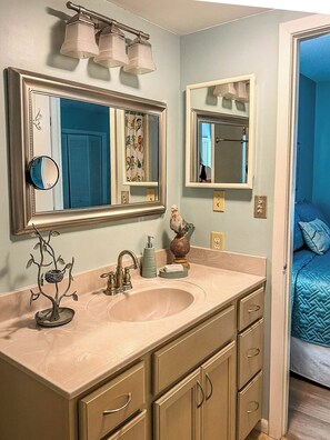 A bathroom with a sink, mirrors, a vanity, and a bed visible through an open door. - Cozy 1 bedroom condo in walking distance to the Club, the Cradle & the Village! (Pinehurst)