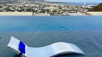A poolside lounge chair with a blue ribbon, overlooking a coastal cityscape with buildings and a clear sky.
