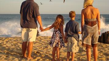 A family holding hands on a sandy beach with waves crashing in the background.
