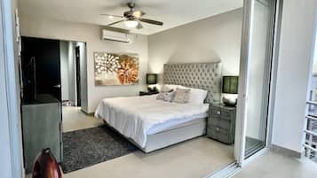 A modern bedroom with a large bed, a ceiling fan, an air conditioning unit, a decorative painting, and a nightstand with a lamp.