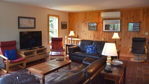 A cozy living room with a television, leather sofas, a wooden coffee table, and a red and blue chair.