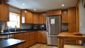 A kitchen with wooden cabinets, a stainless steel refrigerator, a microwave, and a wooden dining table.