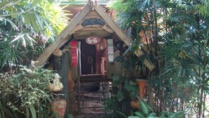 A rustic wooden structure with a triangular roof, surrounded by lush tropical plants. - Baan Suan Jantra Home Stay (Chiang Rai)