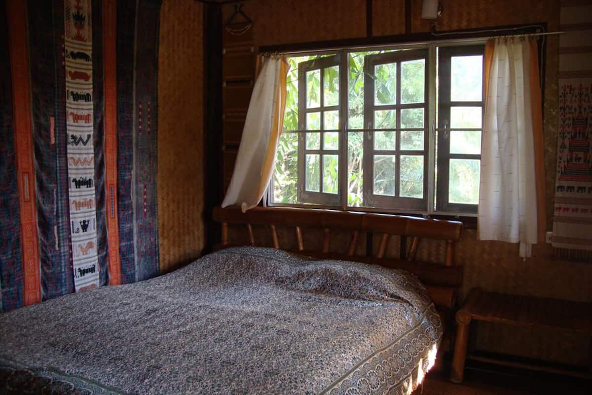 A room with a bed, a window with curtains, and a wall with patterned fabric.