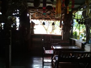 A dimly lit interior with rustic wooden furniture, a large window with a view of trees, and hanging decorations.