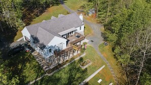 An aerial view of a house with a deck, a driveway, and surrounding trees.