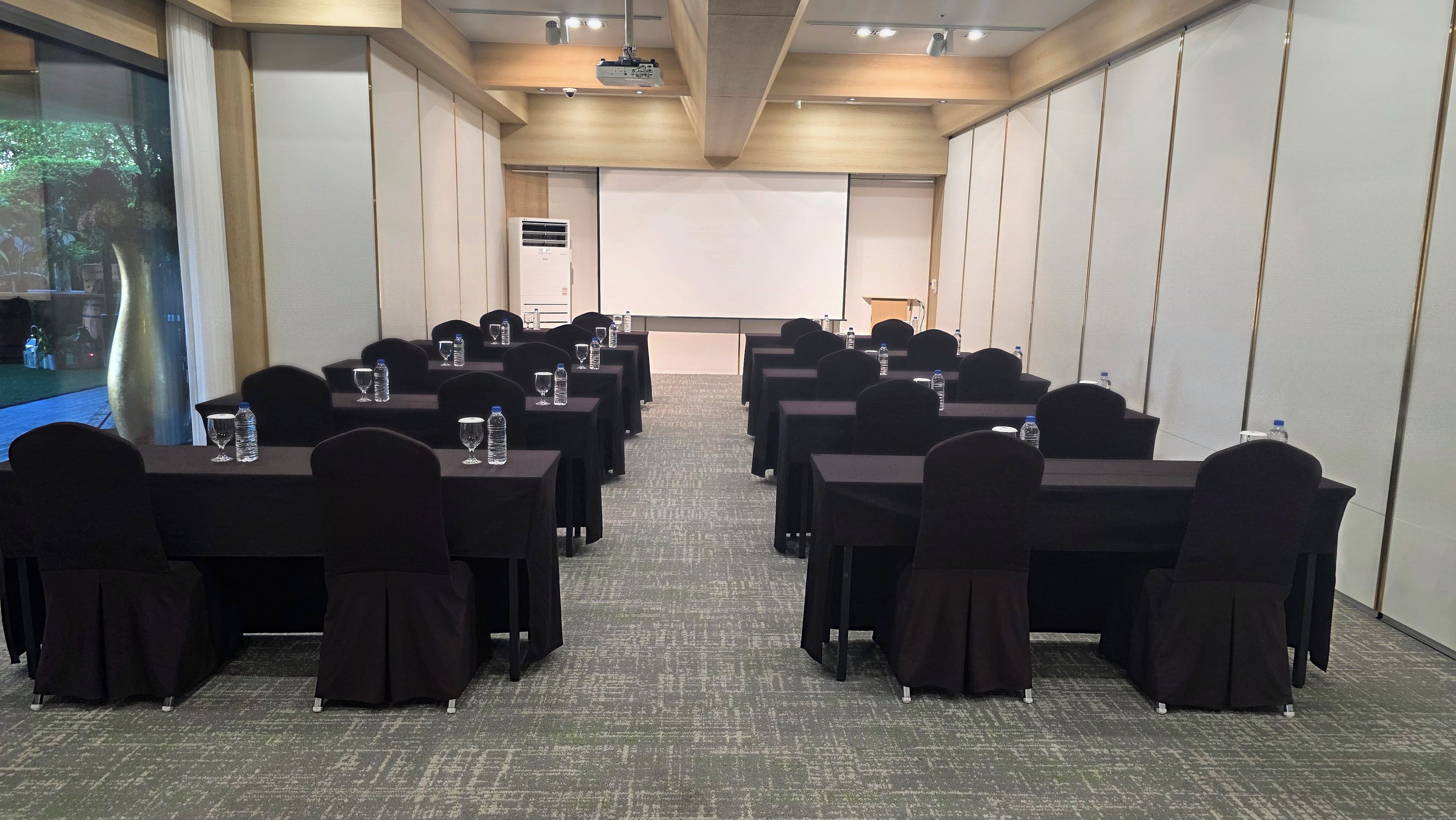 A conference room with rows of tables, chairs, and a projector screen.