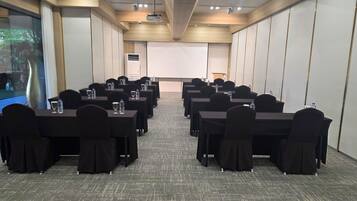 A conference room with rows of tables, chairs, and a projector screen.