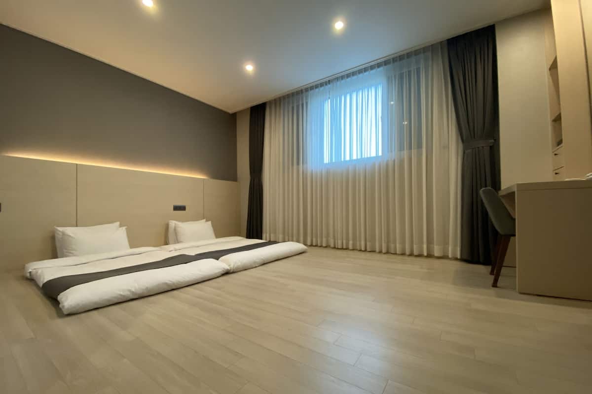 A modern hotel room with a large bed, a desk, and a window with curtains.
