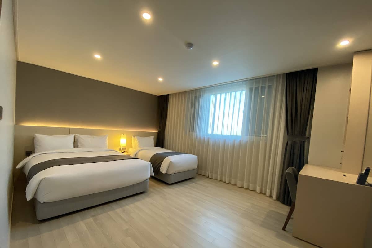 A hotel room with two beds, a desk, and a large window with curtains.