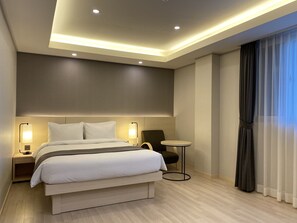 A modern hotel room with a large bed, bedside lamps, a small round table, and a view of the outside through sheer curtains. - New Donghae Hotel (Donghae)
