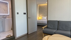 Una habitación de hotel moderna con un sofá gris, una mesa de madera y una cama con cabecera estampada.