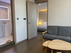 A modern hotel room with a grey sofa, a wooden table, and a bed with a patterned headboard. - New Donghae Hotel (Donghae)