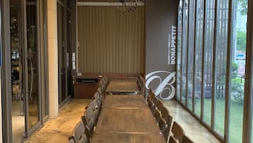 A long wooden table with chairs, a chandelier, and large windows.