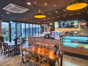 A café interior with wooden furniture, a counter with a coffee machine, and a menu board. - New Donghae Hotel (Donghae)