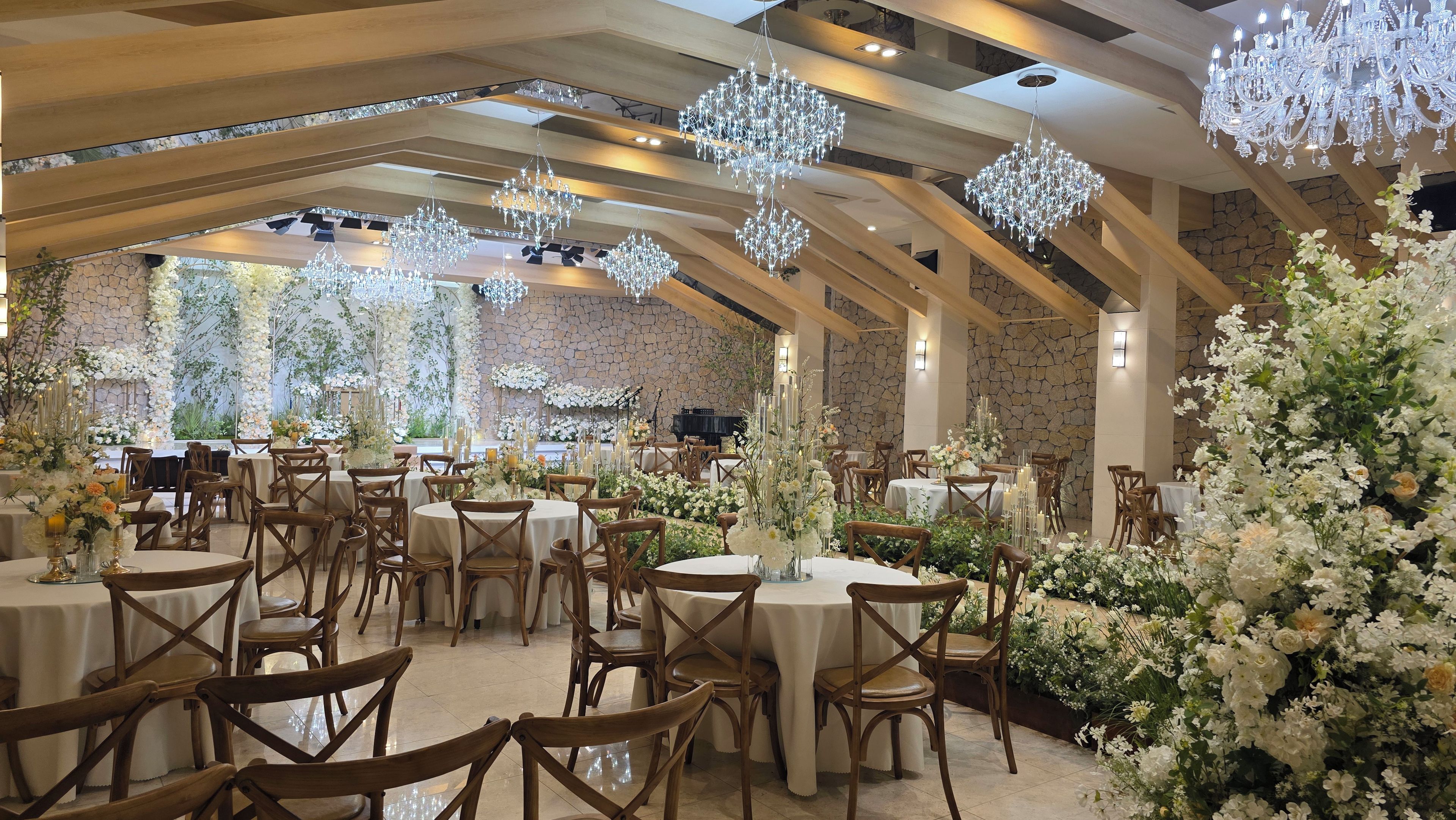 A banquet hall with round tables, wooden chairs, and hanging crystal chandeliers.