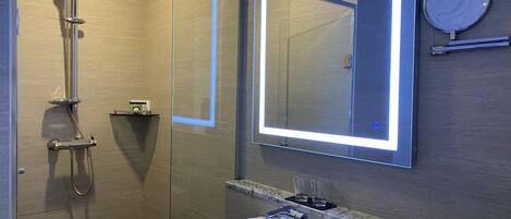 Un baño moderno con ducha acristalada, lavamanos blanco e iluminación integrada en el espejo.